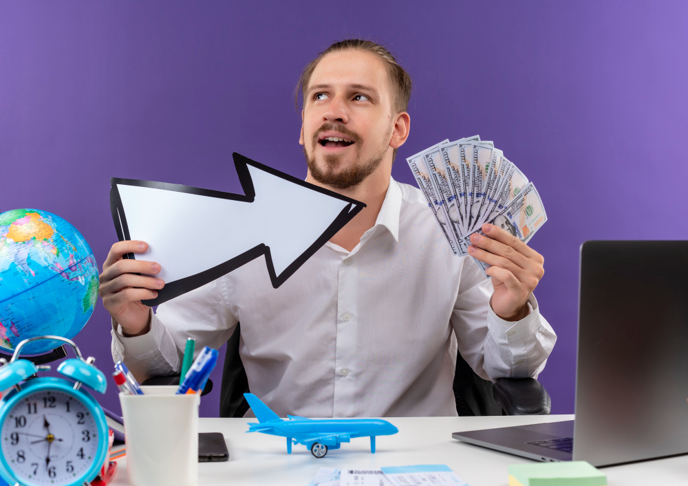 handsome businessman white shirt holding white arrow showing cash looking aside with smile face sitting table offise purple background